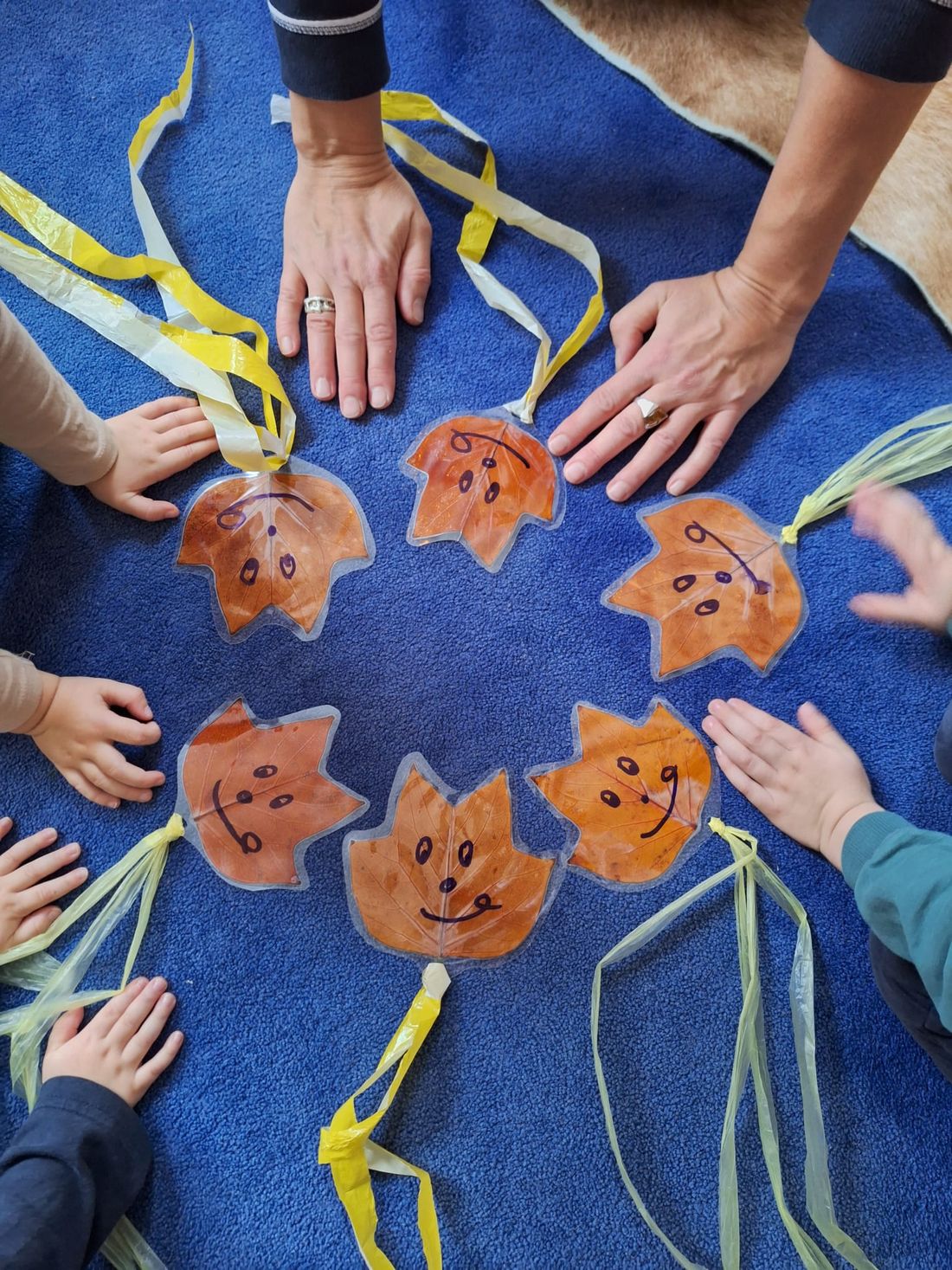 Kinderhände und Erwachsenenhände im Kreis um selbst gebastelte Herbstblätter mit lachenden Gesichtern