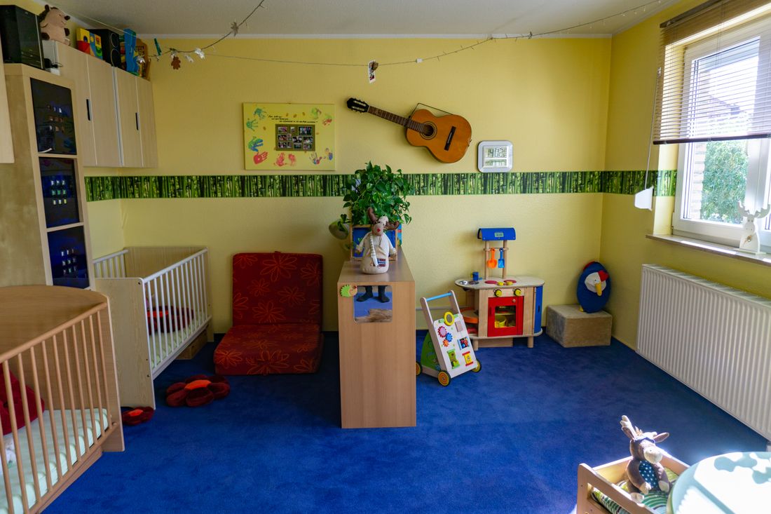Helles Spielzimmer mit blauem Teppich, Kinderbetten, Spielküche, Lauflernwagen und Gitarre an der Wand