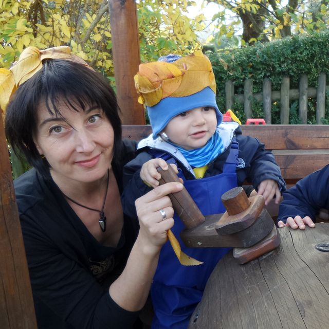 Katrin Starke mit zwei Tageskindern am Holztisch im Garten, die Kinder tragen gebastelte Kronen